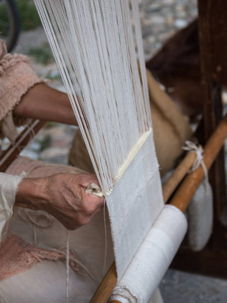 istock Elderly Woman's Hands Weaving White Pattern on Old Wooden Loom 951969578