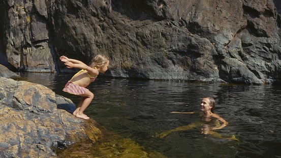 a little girl during a family hike in the mountains collects water from a mountain river in her palm