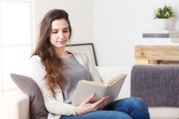 istock Woman reading a book sitting on a couch at home 951983416