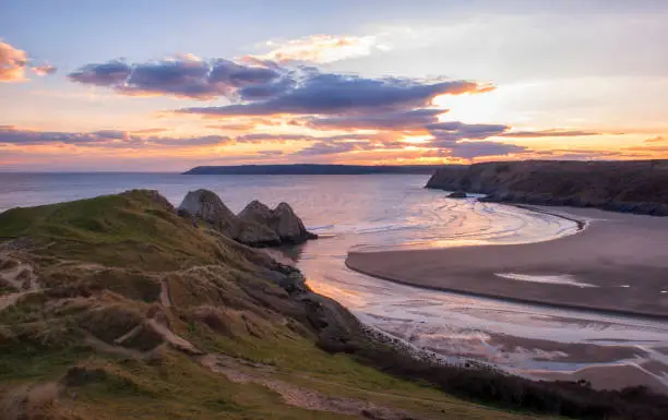 landscape image of three cliffs bay at sunset with the tide in