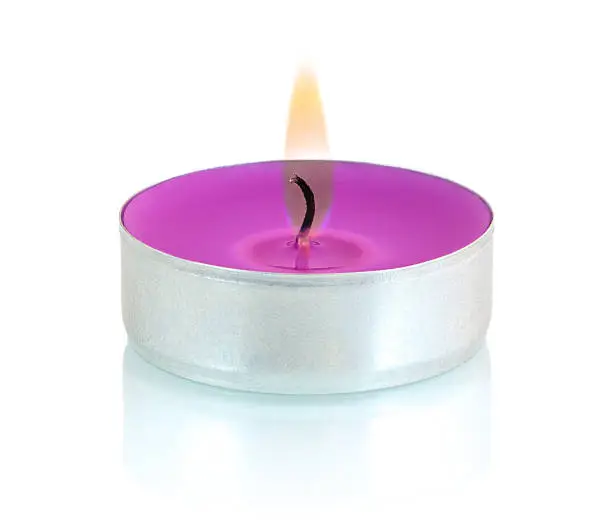 Typical aluminium burning purple tealight candle isolated on white background with shadow reflection. Violet candle with flame and black wick. Tea candle with burning ingle and burned candlewick.