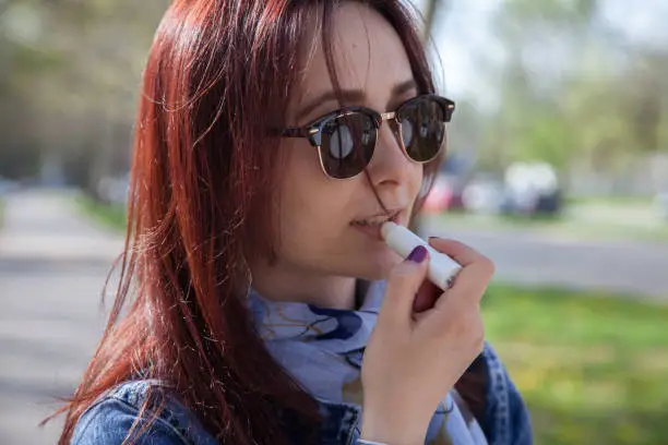 Close-up shot of a young woman applying lip balm while strolling along the city on a sunny day.