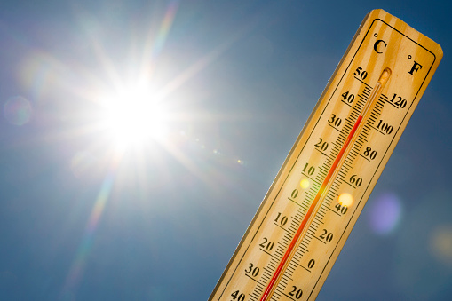 Mercury thermometer marking 39 degrees Celsius 100 Fahrenheit in a sunny day. Summer heat shown on mercury thermometer against the blue sky. Sunlight with sun flares.