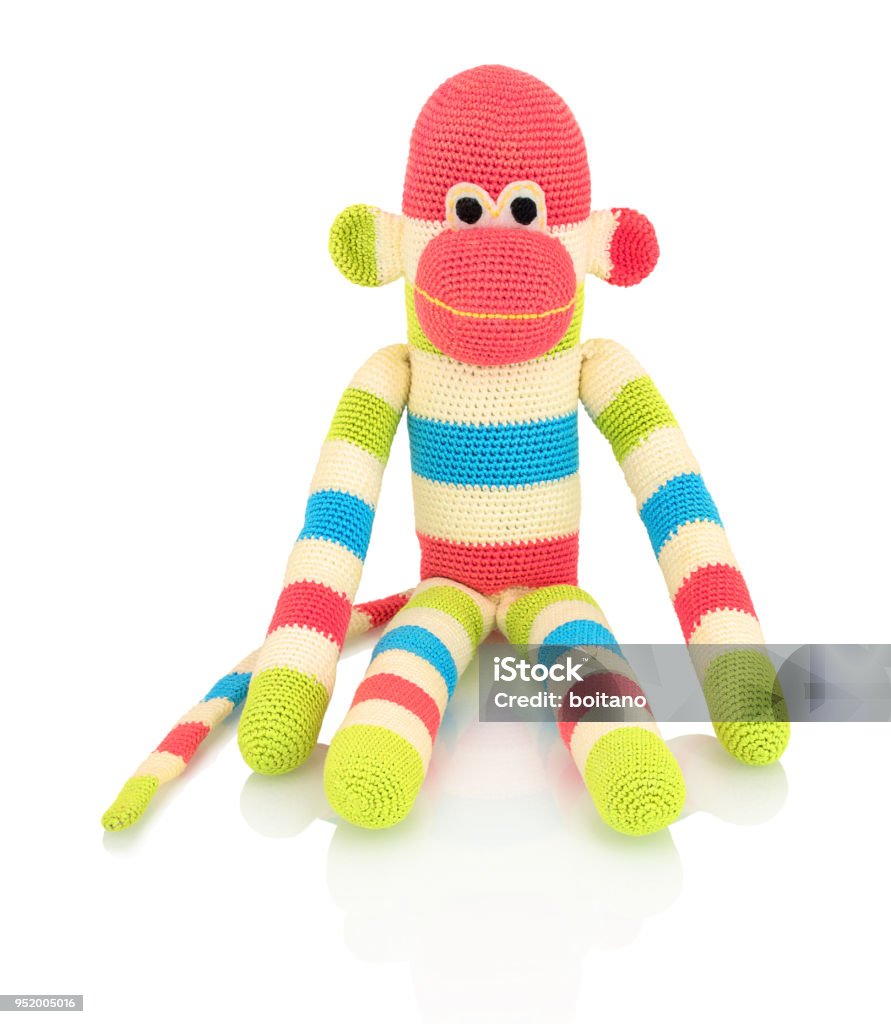 Cute handmade crochet monkey doll isolated on white background with shadow reflection. Playful crochet green pink blue white monkey sitting on white underlay. Knitted ape. Cut Out Stock Photo