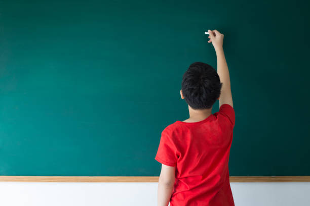 education concept Asian boy writing on empty green board in class room at school writing on chalk board stock pictures, royalty-free photos & images