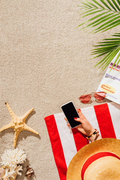 cropped shot of woman using smartphone while relaxing on sandy beach