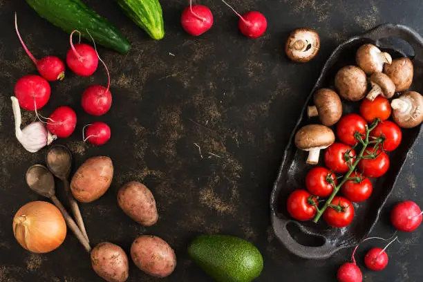 Photo of Varied vegetables and mushrooms on a rustic ceramic dish. Dark brown background, top view, empty center for text.