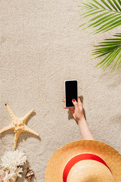 istock cropped shot of woman in hat using smartphone while lying on sandy beach 952012372
