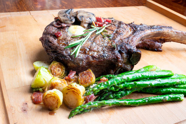 Huge Cowboy Cut Rib Eye Beef Steak with Ketogenic Vegetables on a Plate Large cowboy cut bone-in rib eye steak grilled up and on a plate with Brussels sprouts and Asparagus, a perfect ketogenic or low carb diet meal. porterhouse steak stock pictures, royalty-free photos & images