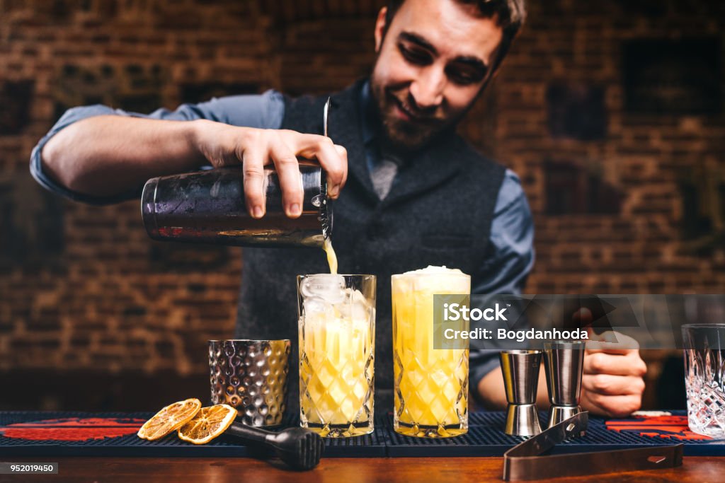 Professional barman preparing cocktails and pouring fresh alcohol in glasses. Cocktails served in bar, restaurant or pub Bartender Stock Photo