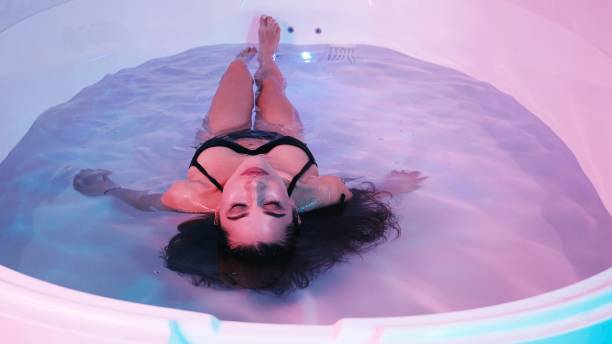 молодая женщина плавает в спа-ванне или бассейне, она очень расслаблена. концепция уэлнесса - floating on water storage tank zero gravity healthy lifestyle стоковые фото и изображения