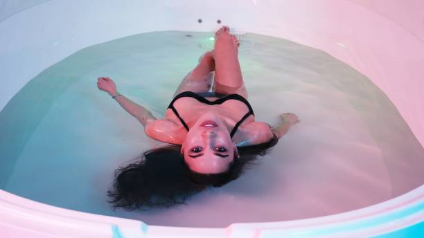 молодая женщина плавает в спа-ванне или бассейне, она очень расслаблена. концепция уэлнесса - floating on water storage tank zero gravity healthy lifestyle стоковые фото и изображения
