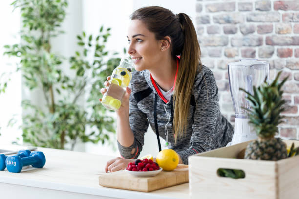 deportiva mujer joven mirando hacia los lados mientras que beber jugo de limón en la cocina en casa. - smoothie fruit drink healthy lifestyle fotografías e imágenes de stock