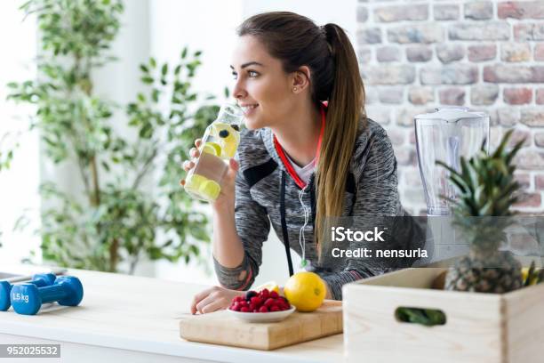 Sporty Young Woman Looking Sideways While Drinking Lemon Juice In The Kitchen At Home - Fotografias de stock e mais imagens de Estilo de vida saudável