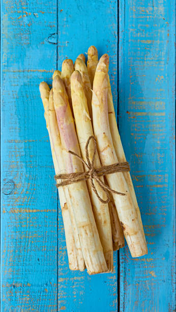 istock Bundle of raw white asparagus over a blue wooden table. 952028964