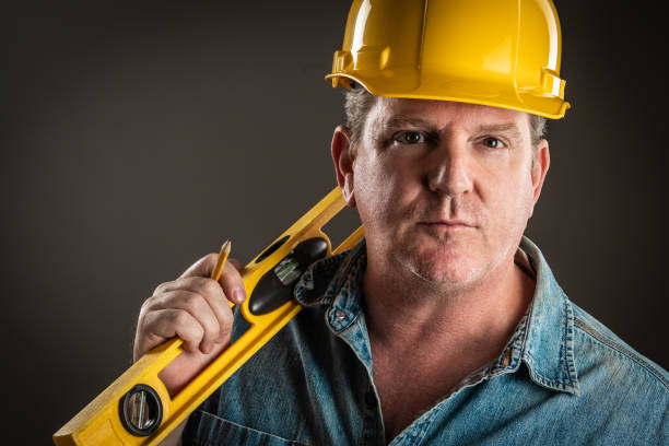 istock Serious Contractor in Hard Hat Holding Level and Pencil With Dramatic Lighting. 952036812
