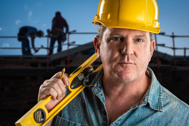istock Serious Contractor in Hard Hat Holding Level and Pencil At Construction Site. 952036916
