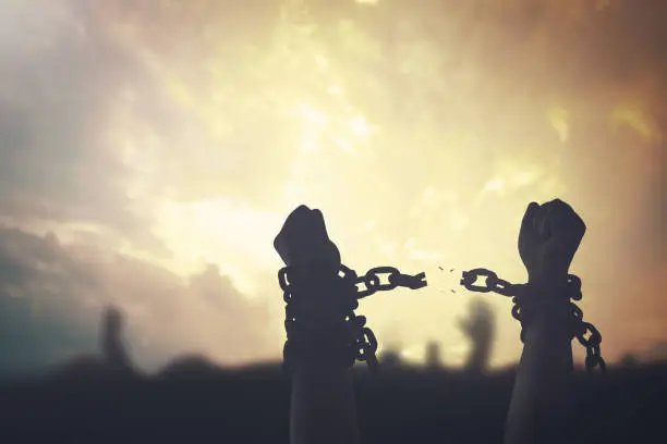 Silhouette human hands raising and broken chains at sunset background