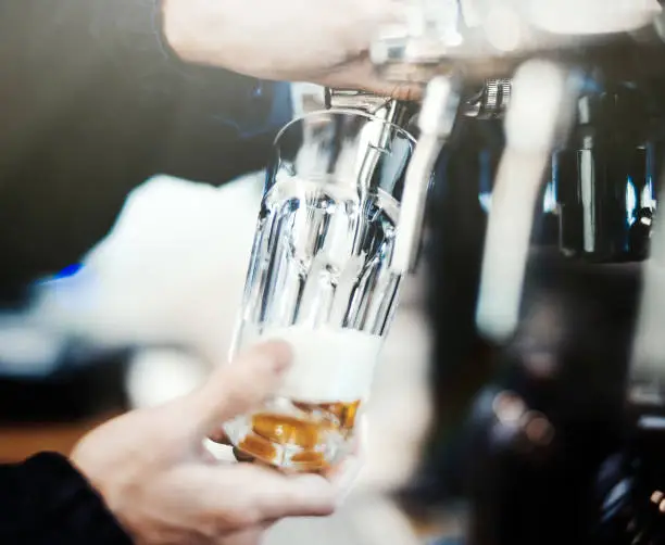 Photo of Bartender man poors glass of beer.