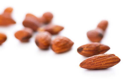 Whole roasted almonds  lightly salted on white background. Selective focus on front almond and the rest are slightly out of focus. White background, healthy eating concept.