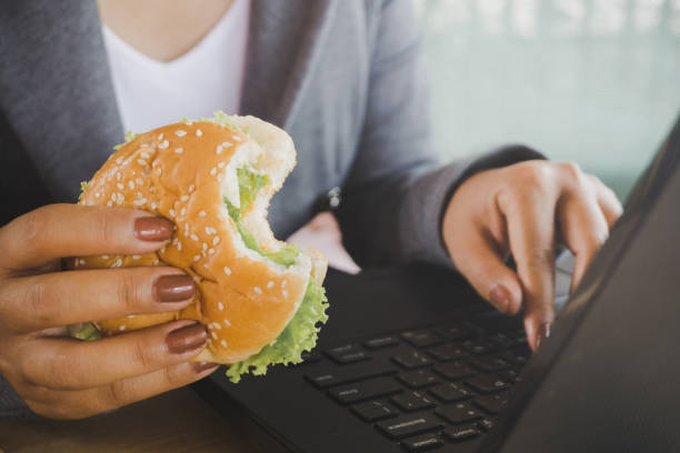 woman eating junk food burger while working on computer laptop
