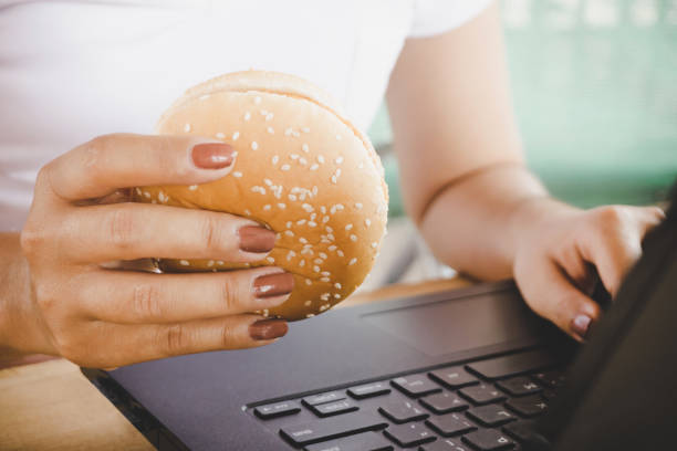 istock woman eating junk food burger while working on computer laptop 952070870