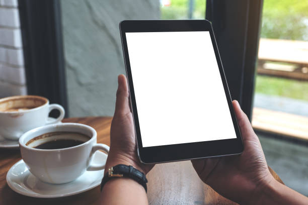 istock Mockup image of hands holding black tablet pc with white blank screen and coffee cups on table 952071472