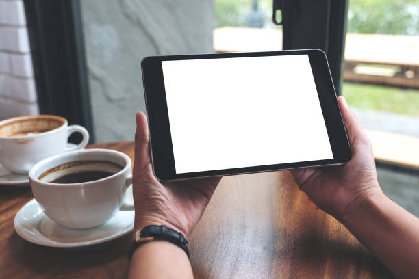 istock Mockup image of hands holding black tablet pc with white blank screen and coffee cups on table 952071536