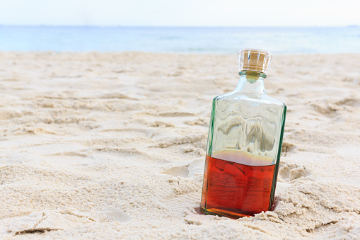 Beverage alcohol is brandy bottle on sand beach background.