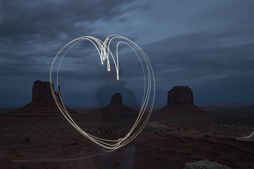 Long exposure showing a person drawing the shape of a heart with a flashlight in front of Monument Valley
