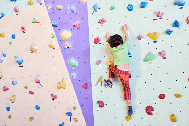 A 4 years old caucasian girl climbing on a gym climbing wall.