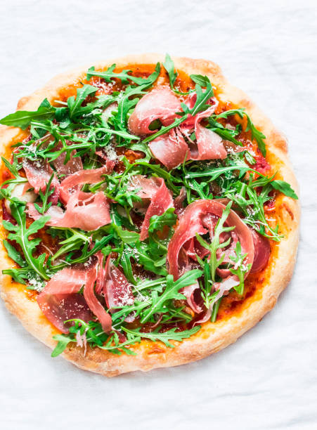 istock Prosciutto arugula homemade pizza on light background, top view. Delicious appetizers, snack, tapas in mediterranean style. Free space 952102350