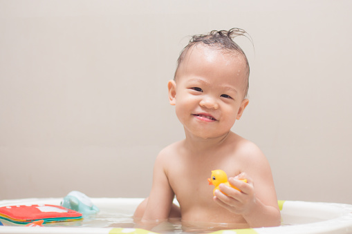 Cute little Asian 18 months / 1 year old toddler baby boy child taking a bath at home, Smiling kid having fun in bath time playing with yellow rubber duck toys, Hygiene care for young children concept