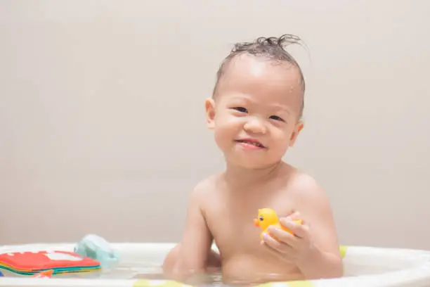 Photo of Asian 18 months / 1 year old toddler baby boy child taking a bath at home, Smiling kid having fun in bath time playing with colorful rubber toy