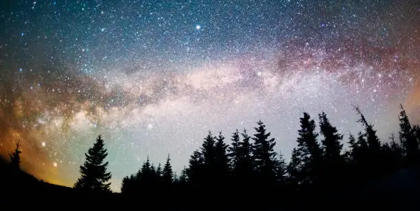 The dark mountain night shines with millions of stars over the fabulous Alpine peak in the Carpathians, the Milky Way of the Galaxy passes over a coniferous forest with a huge arc