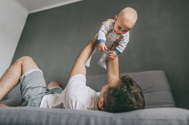 istock young father lying on sofa and playing with cute infant child 952110176