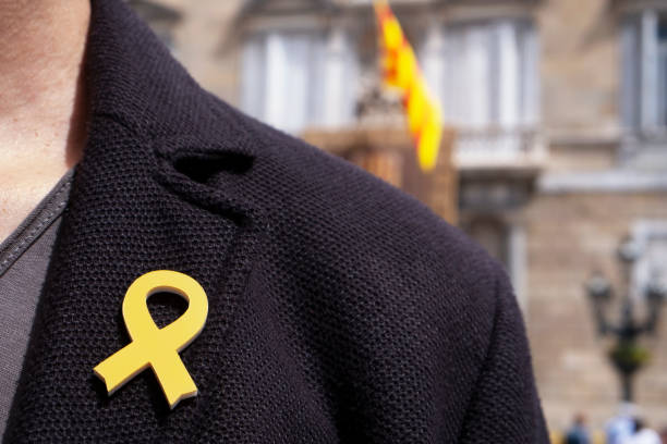 young man with a yellow ribbon pinned in the flap of his jacket in front of the Palau de la Generalitat de Catalunya, the seat of the Government of Catalonia in Barcelona, Spain