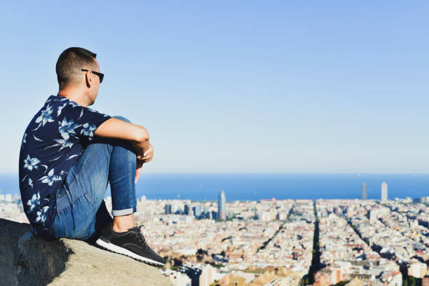 closeup of a young caucasian man, seen from behind, at the top of a hill observing the city of Barcelona, Spain, below him