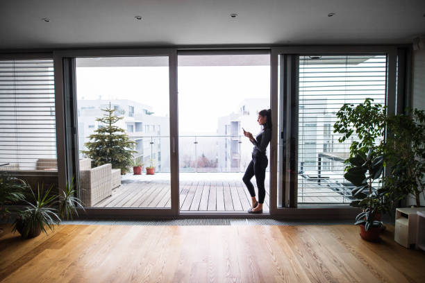 donna vicino alla finestra con smartphone, sms. - blinds apartment living room contemporary foto e immagini stock