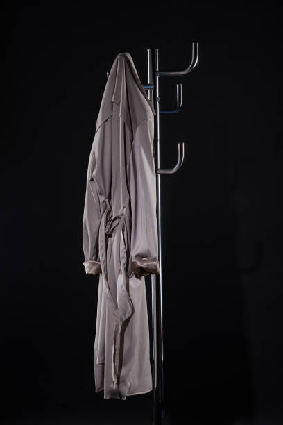 траншеи пальто висит на пальто стойку изолированы на черном - coat coat hook hatstand hanging стоковые фото и изображения