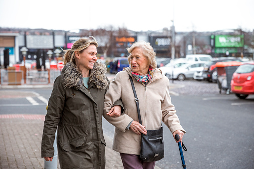 A mature woman help a senior woman out of a car as she takes her to the shops