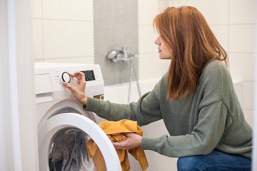 Young woman doing laundry, setting a washing machine. About 25 years old, Caucasian female.