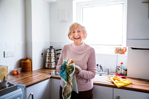 Senior woman looking happy as she stands in her kitchen drying dishes.