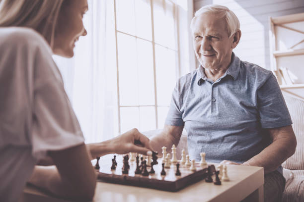 Volunteer and old people Beautiful young girl-volunteer and handsome old man are playing chess and smiling senior chess stock pictures, royalty-free photos & images