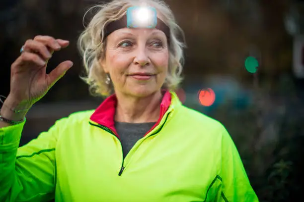 A portrait of a mature female urban runner wearing a head torch