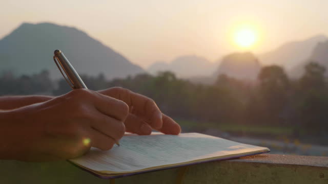 Young woman writing morning pages in diary outdoor, close-up in slow motion