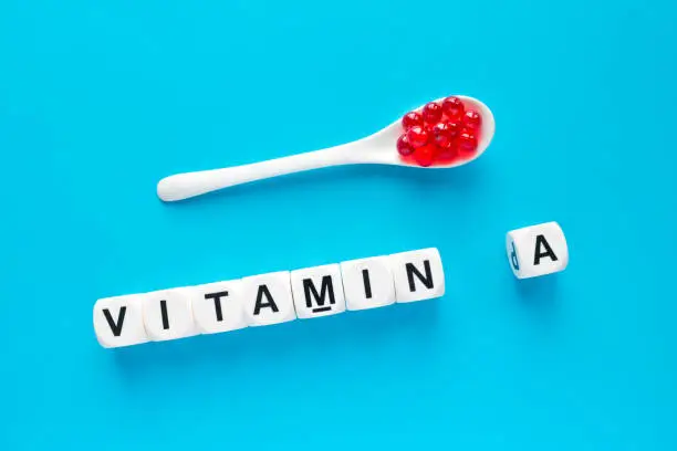 Photo of Red capsules in the white spoon and the word vitamin A from white cubes