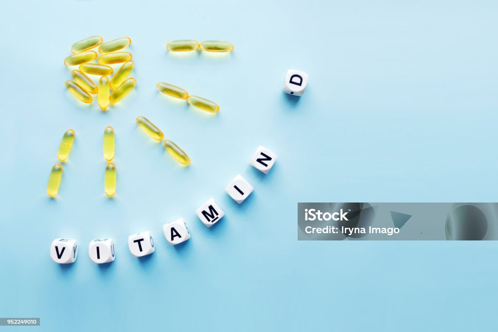 Yellow capsules in the form of the sun with rays and the word vitamin D from white cubes Yellow capsules in the form of the sun with rays and the word vitamin D from white cubes with letters on a blue background. VITAMIN D word for healthy and medical concept. Sunshine vitamin health benefits Vitamin D Stock Photo