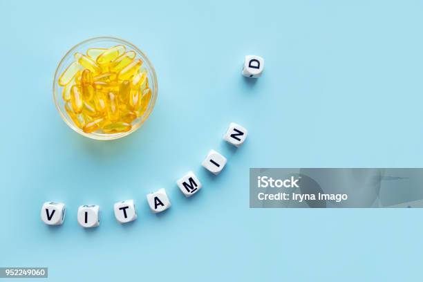 Yellow Capsules In The Round Glass Bowl And The Word Vitamin D From White Cubes With Letters On A Blue Background Stock Photo - Download Image Now