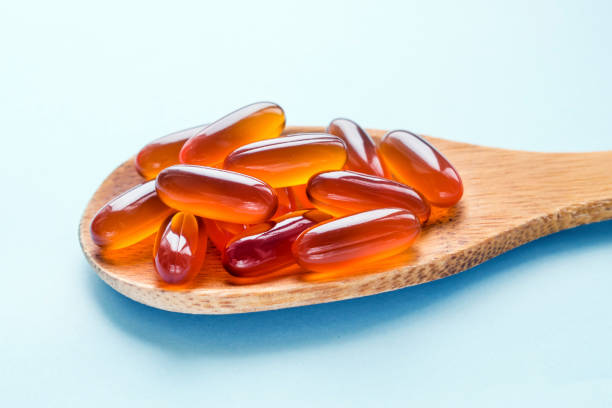 tabletki żelowe lecytyny w drewnianej łyżce wyizolowanej na niebieskim jasnym tle - vitamin pill nutritional supplement capsule lecithin zdjęcia i obrazy z banku zdjęć